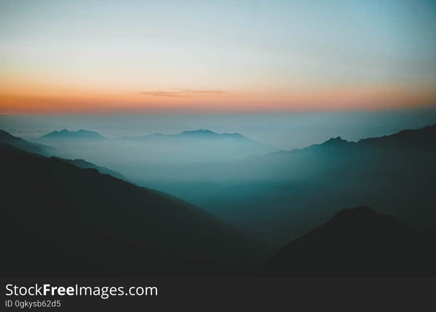 Mountain peaks on a foggy day with the sunset on the horizon.