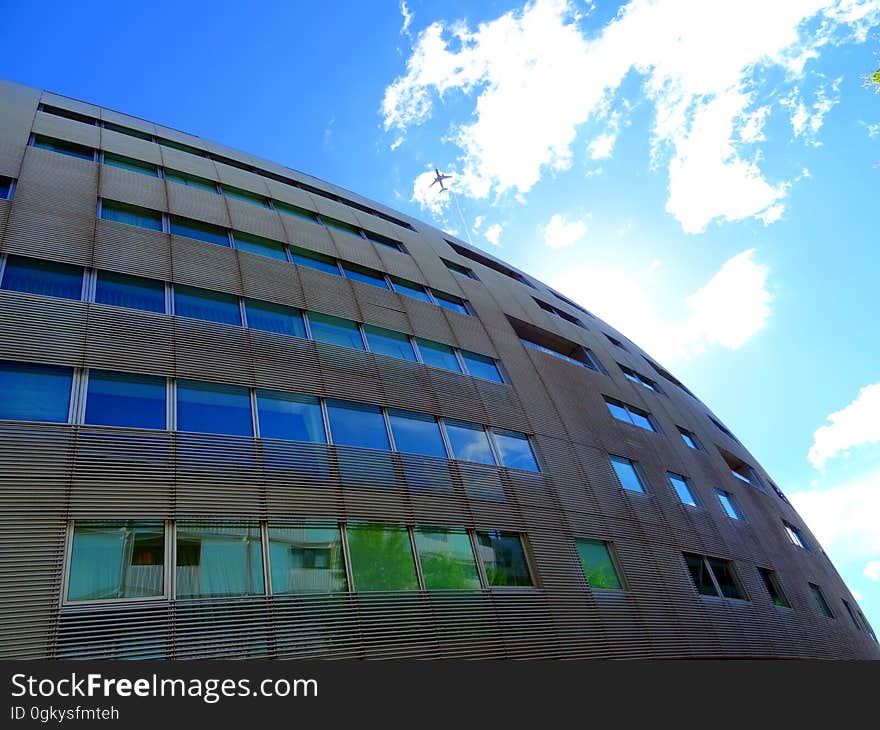 Glass and concrete building (apartments or offices) architecturally designed with a curved facade and with reflections of the blue sky and on lower floor of green trees. Glass and concrete building (apartments or offices) architecturally designed with a curved facade and with reflections of the blue sky and on lower floor of green trees.