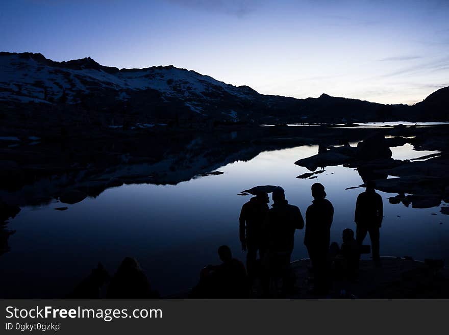 A group of people stand around a lake at twilight. A group of people stand around a lake at twilight.