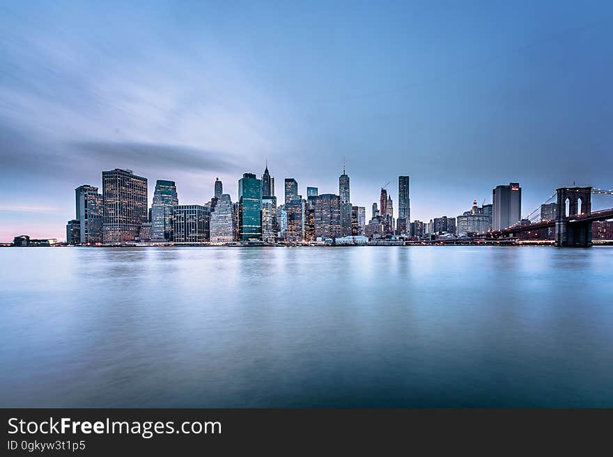 Skyscrapers of Manhattan, New York skyline against blue skies at sunrise over riverfront with Brooklyn Bridge. Skyscrapers of Manhattan, New York skyline against blue skies at sunrise over riverfront with Brooklyn Bridge.