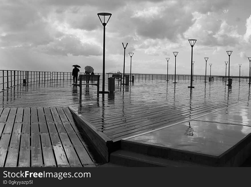 Tourists using umbrellas standing on rainy boardwalk in black and white. Tourists using umbrellas standing on rainy boardwalk in black and white.