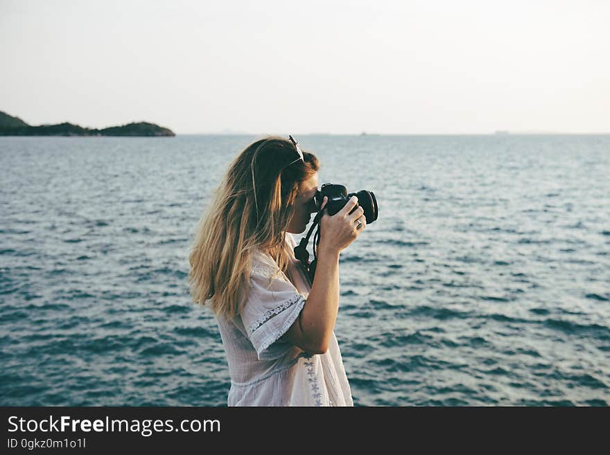 A woman standing on a beach with a camera taking photos. A woman standing on a beach with a camera taking photos.