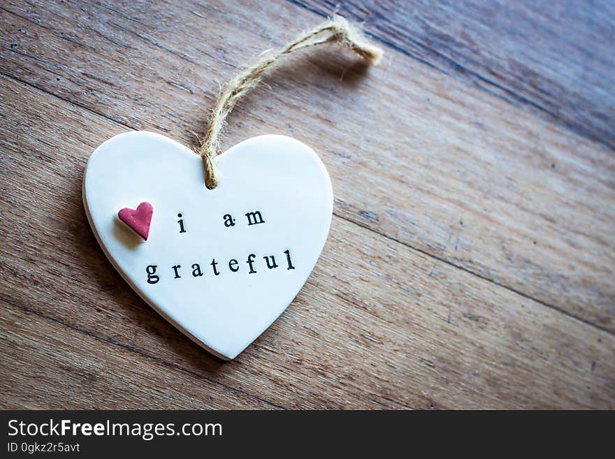 Close up of white china heart ornament with message i am grateful on rustic wooden boards.