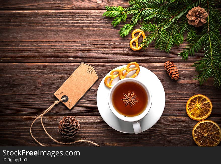 Christmas still life with green pine boughs, pine cones, orange slices and cup of tea in white cup and saucer on rustic wooden boards with blank gift tag. Christmas still life with green pine boughs, pine cones, orange slices and cup of tea in white cup and saucer on rustic wooden boards with blank gift tag.