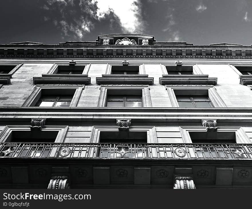 Front of apartment building with balconies and window against cloudy skies in black and white.