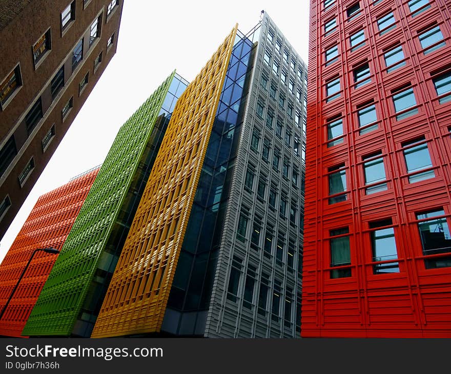 High rise buildings in the city constructed of glass, concrete and steel all in different colors, red, yellow, green, orange and brown, pale sky. High rise buildings in the city constructed of glass, concrete and steel all in different colors, red, yellow, green, orange and brown, pale sky.