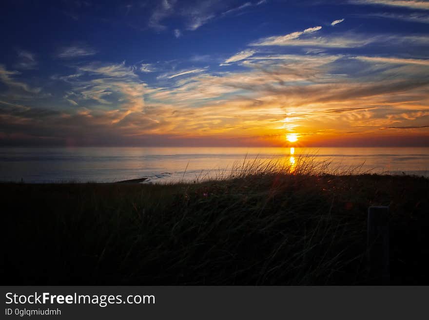 Sunset in orange skies over dunes on sandy coastline. Sunset in orange skies over dunes on sandy coastline.