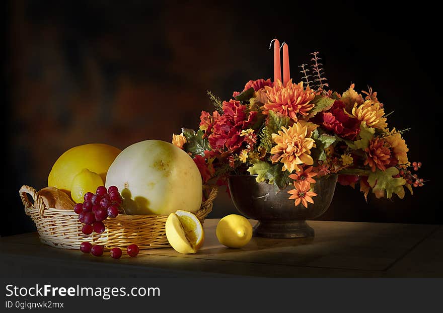 An autumn flower arrangement sitting next to a fruit basket. An autumn flower arrangement sitting next to a fruit basket.