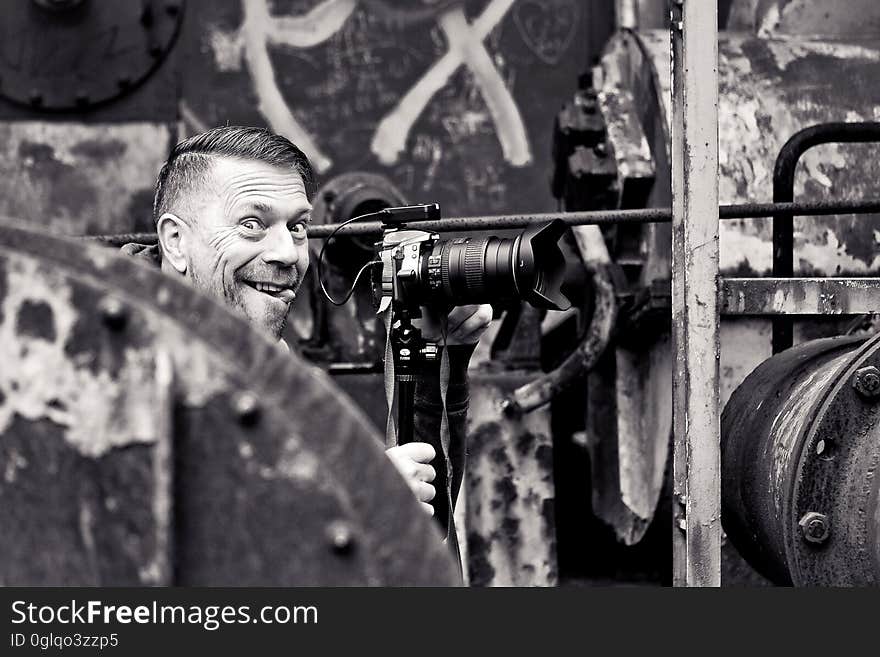 Smiling male photographer surrounded by industrial equipment in black and white. Smiling male photographer surrounded by industrial equipment in black and white.