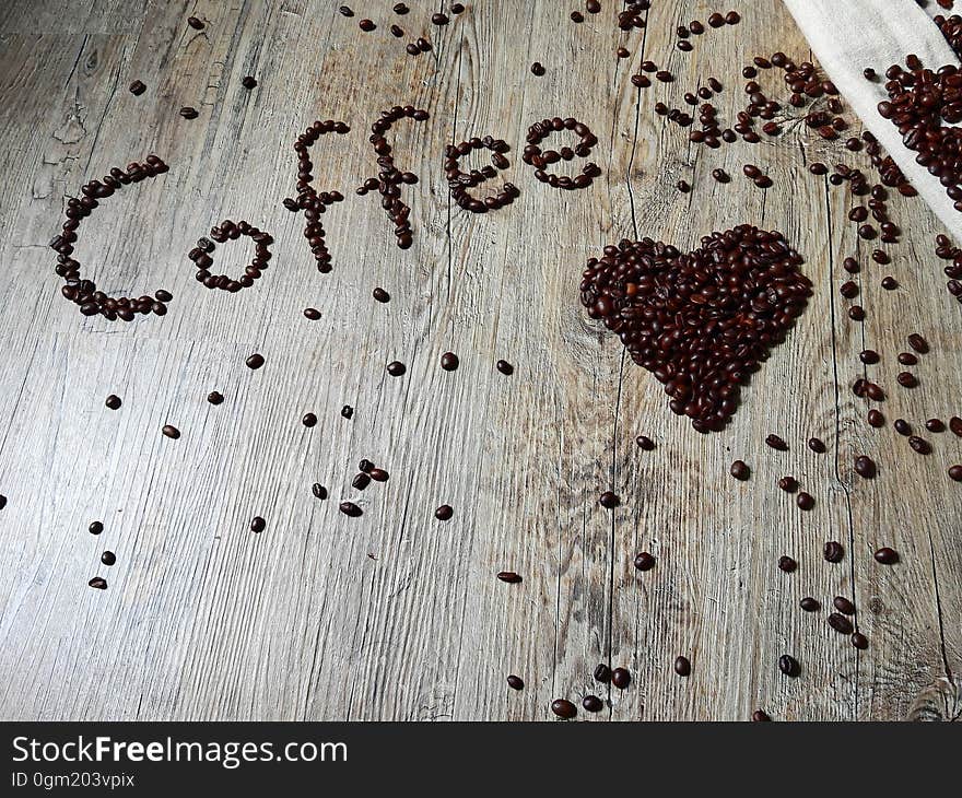 Coffee beans on a wood surface forming the word "coffee" and a heart shape.