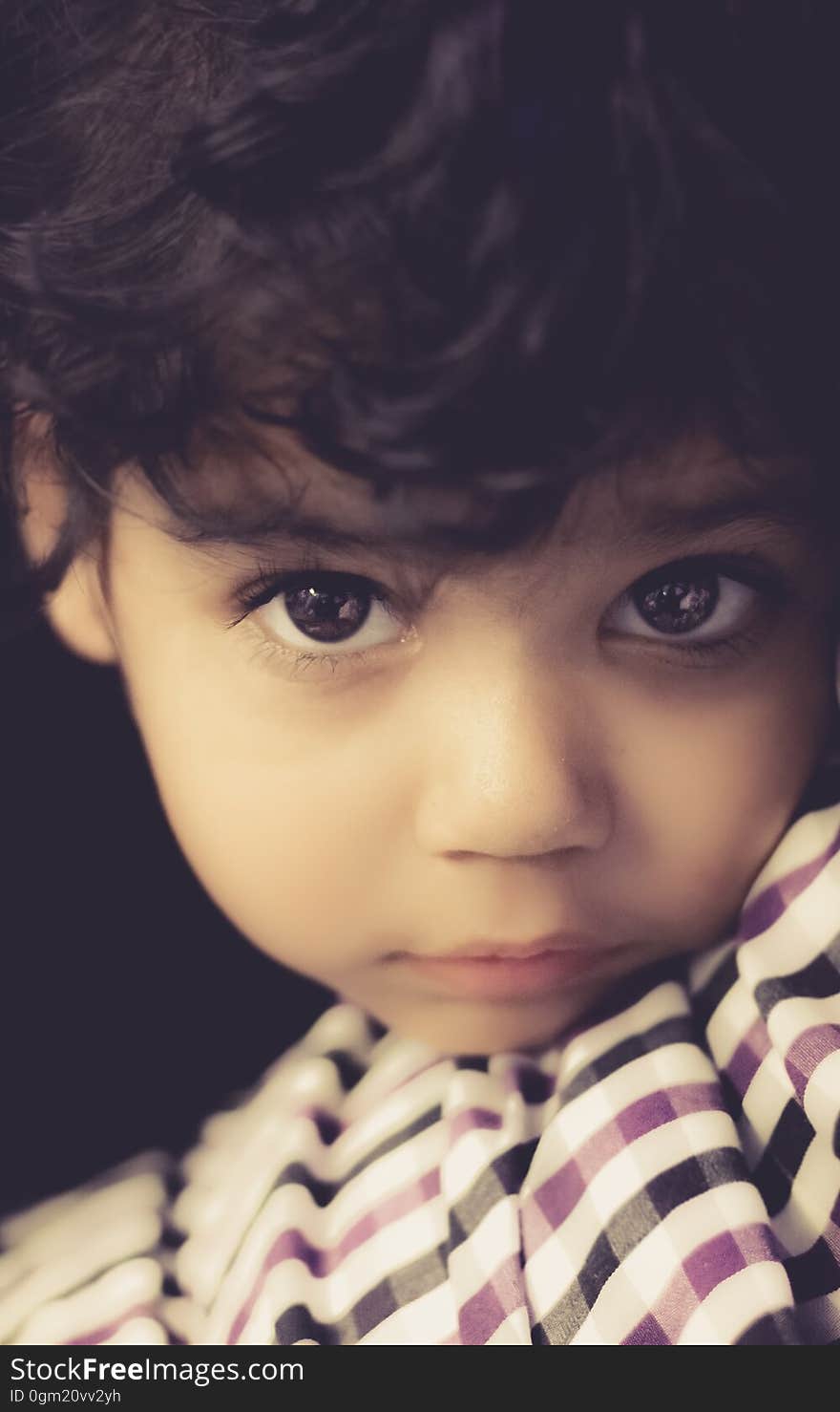 Portrait of young boy with brown curly hair and brown eyes leaning on striped pillow.