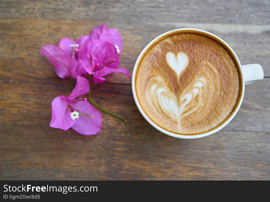 Overhead of cup of latte with heart shapes in froth with purple flowers on wooden tabletop. Overhead of cup of latte with heart shapes in froth with purple flowers on wooden tabletop.