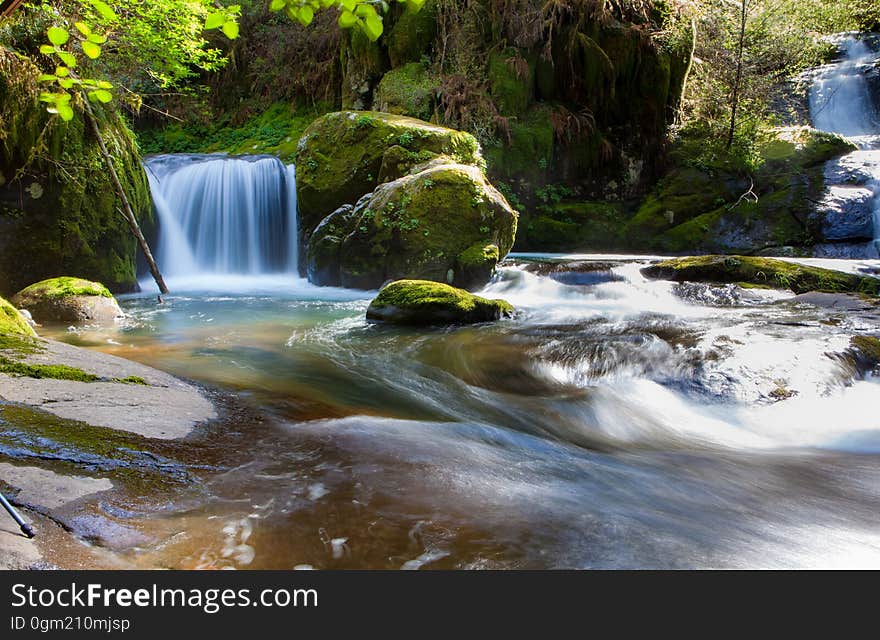 Waterfall over rocks in stream though green forest. Waterfall over rocks in stream though green forest.