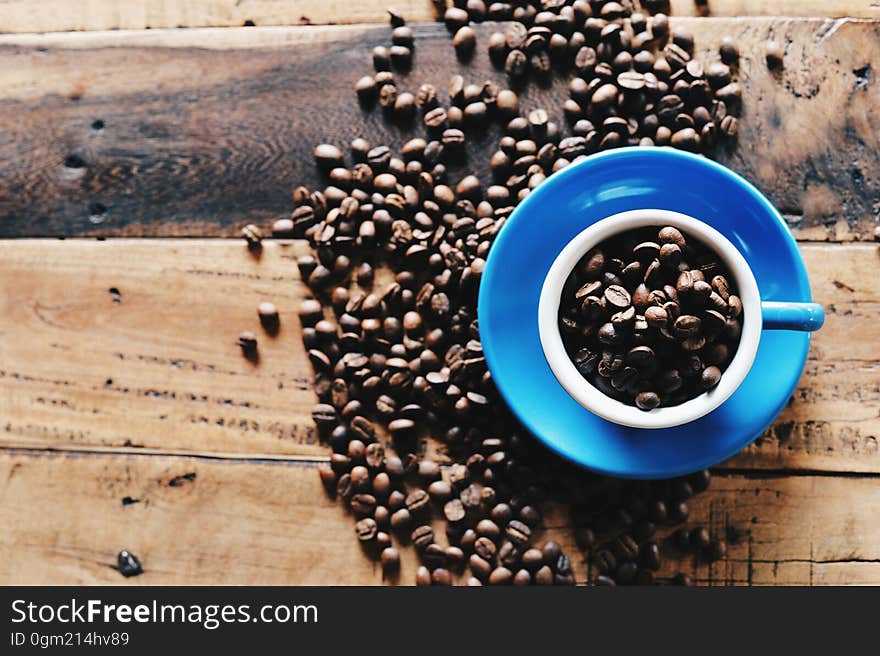 Overhead of coffee beans in blue cup and saucer on rustic wooden boards.