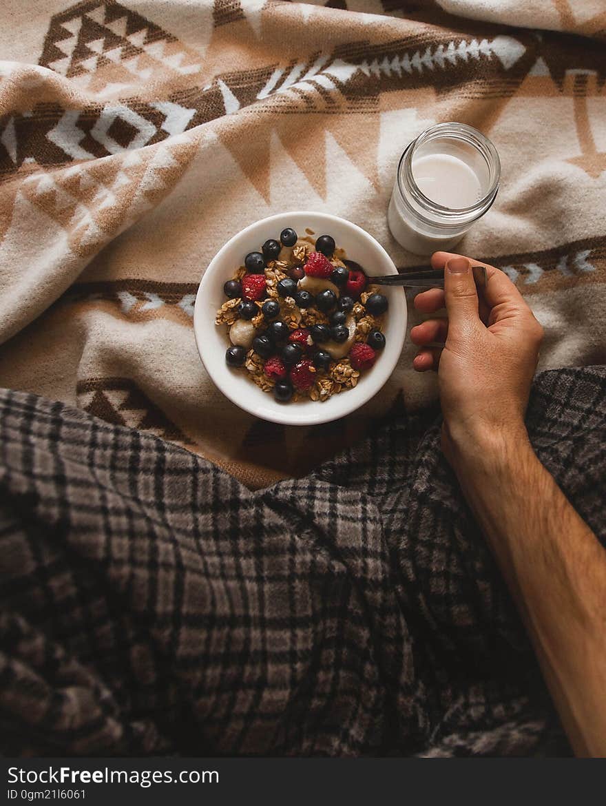 Hand holding spoon in bowl of muesli with glass of milk on Indian blanket. Hand holding spoon in bowl of muesli with glass of milk on Indian blanket.