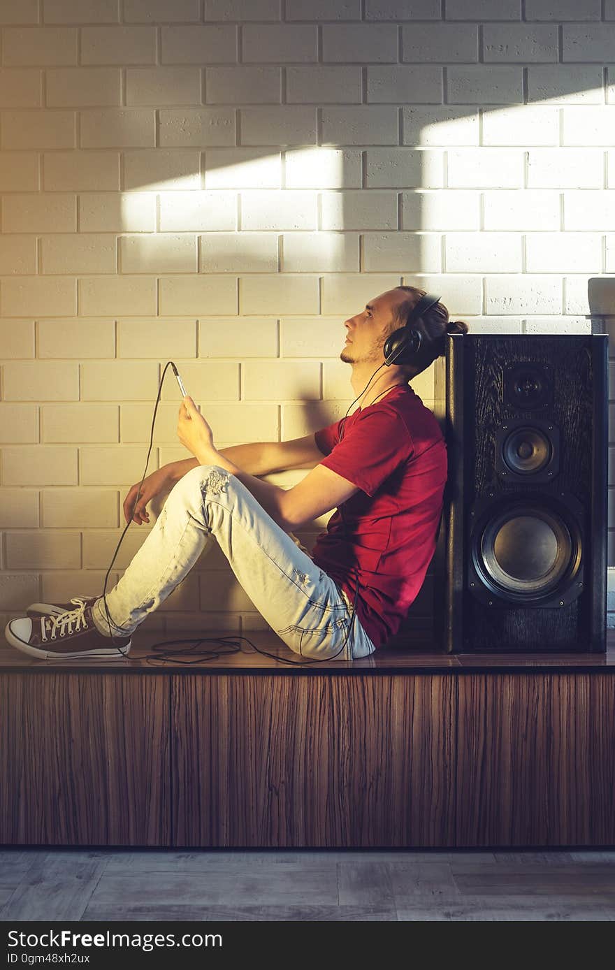 Handsome man, a music lover listens to music with headphones with a mobile phone in a modern interior against the media and large speakers. Enjoying music is fun and communicates on the Internet at home. The concept of creative and positive lifestyle. Handsome man, a music lover listens to music with headphones with a mobile phone in a modern interior against the media and large speakers. Enjoying music is fun and communicates on the Internet at home. The concept of creative and positive lifestyle