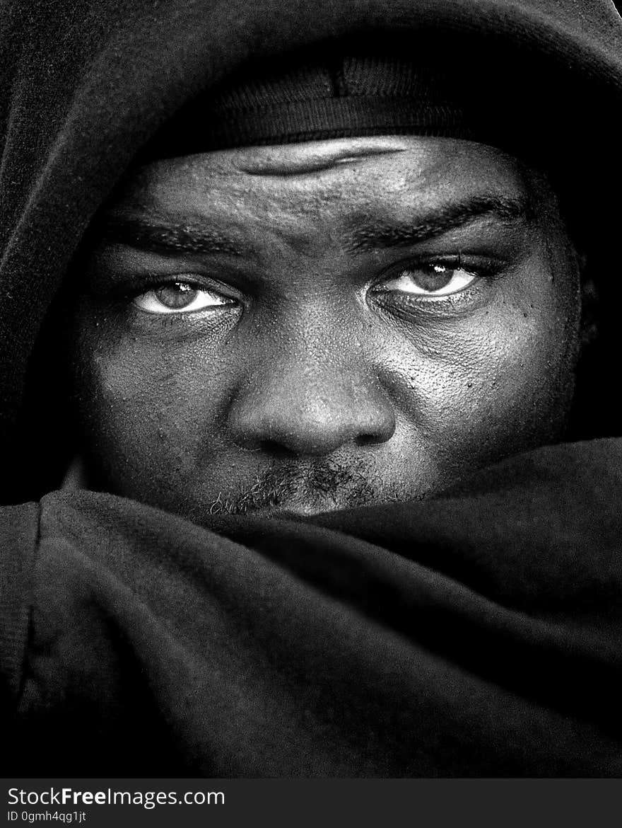 Studio portrait of African man wearing hat and hood in black and white with serious expression.