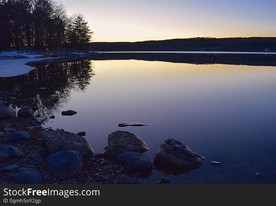 Lights of sunset reflecting in calm waters from rocky shores.