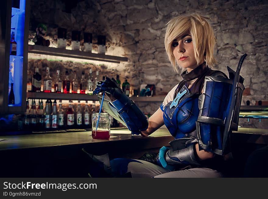 Woman in Blue and Black Mascot Sitting Near Drinking Glass