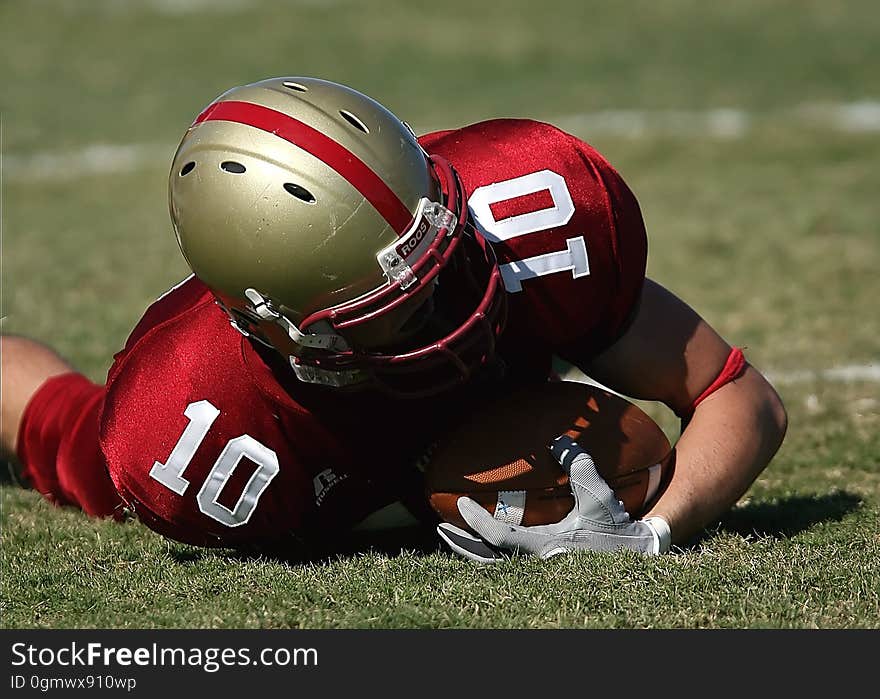 Man in Red White Football Jersey and Grey Red Helmet Holding Football and Lying on Green Grass Field