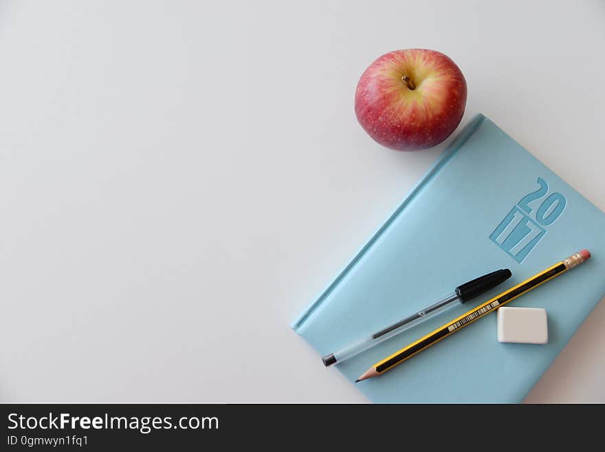 A yearly planner with pens next to an apple.