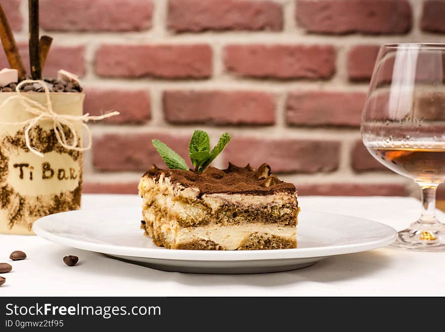 A slice of tiramisu next to a glass of brandy.