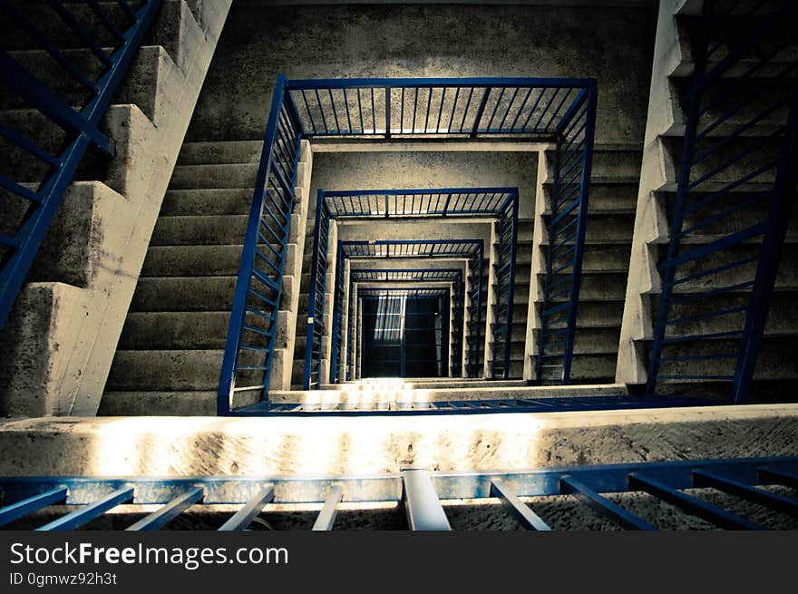 View down a concrete staircase covering many floors with safety railings for a building under construction. View down a concrete staircase covering many floors with safety railings for a building under construction.