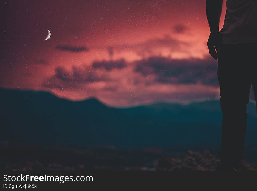 A silhouette of a person watching a crimson sky as night falls.