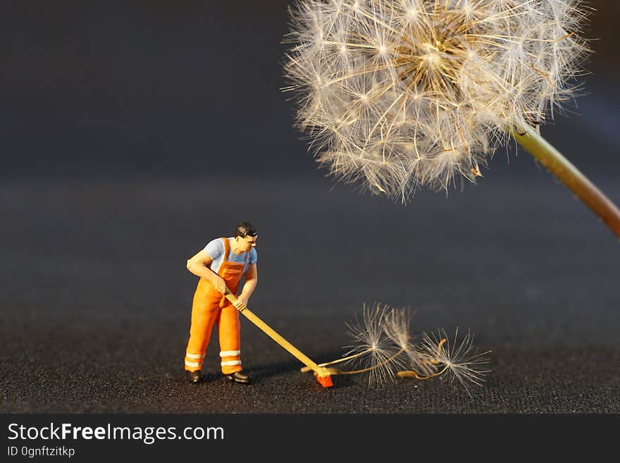 A toy figurine posed to sweep up dandelion seeds. A toy figurine posed to sweep up dandelion seeds.