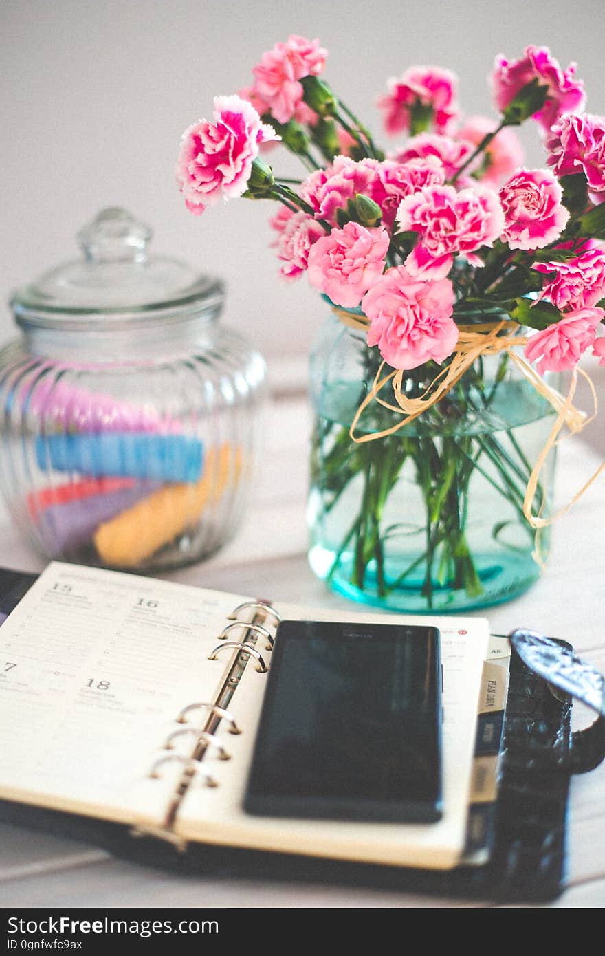 A journal with a mobile phone on a table with a bouquet of carnations. A journal with a mobile phone on a table with a bouquet of carnations.