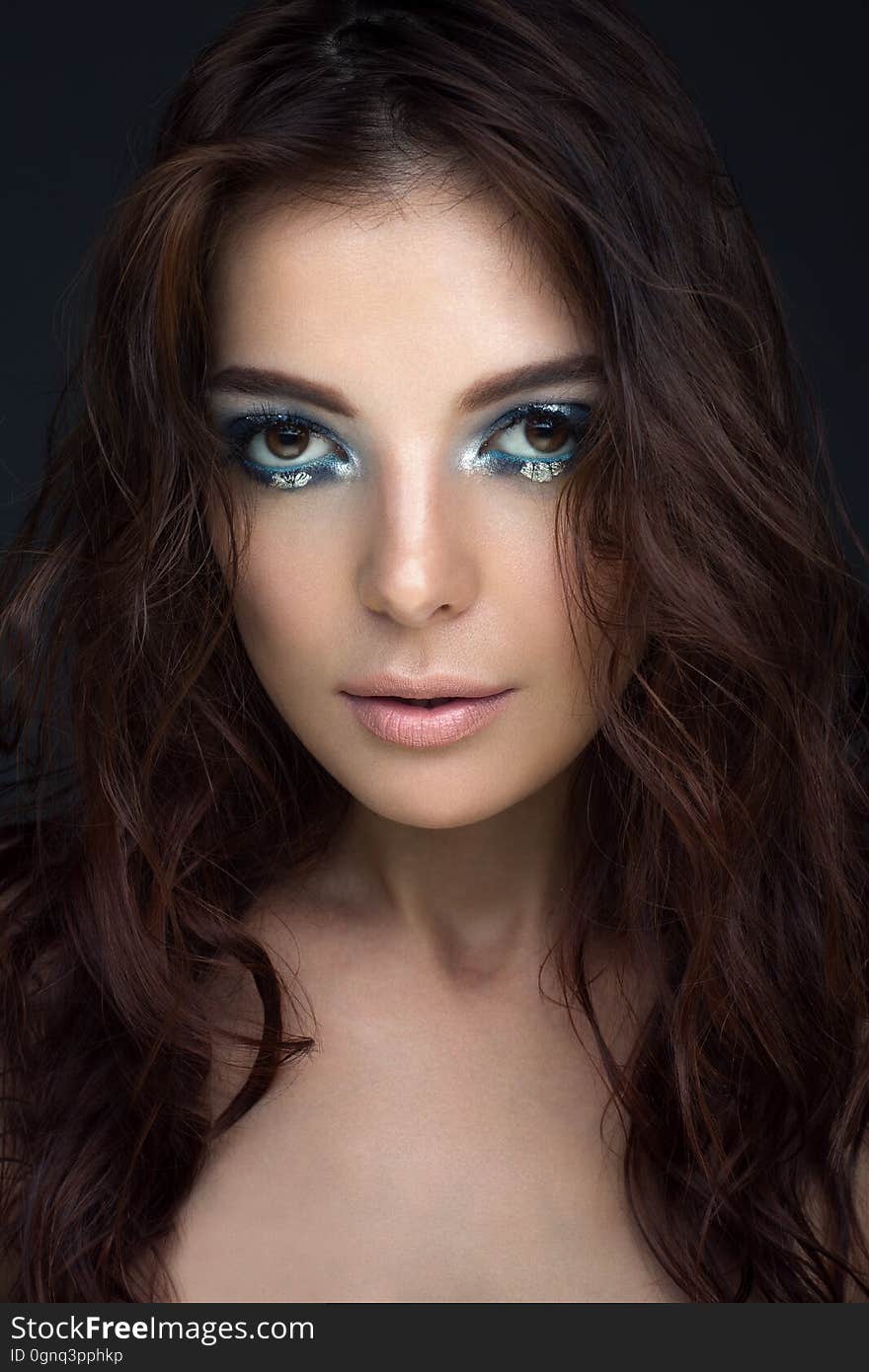 Close-up portrait of girl with dark hair with blue eyeshadow and silver dots, looking at the camera. Vertical photo