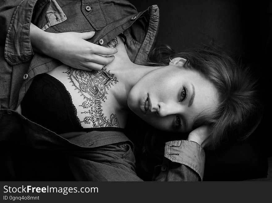 Black and white portrait of a girl in a denim shirt and black bra with a mehendi on her chest lying on the sofa, top view.