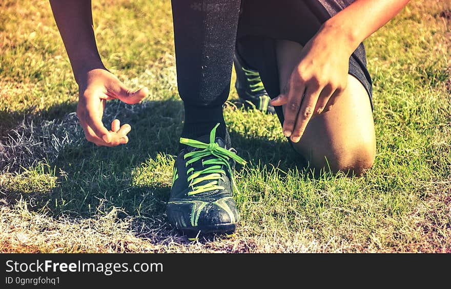 Man kneeling in grassy sports field wearing athletic shoes. Man kneeling in grassy sports field wearing athletic shoes.