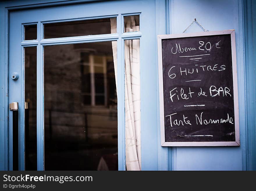 Chalkboard sign with specials outside restaurant on blue wall next to window. Chalkboard sign with specials outside restaurant on blue wall next to window.