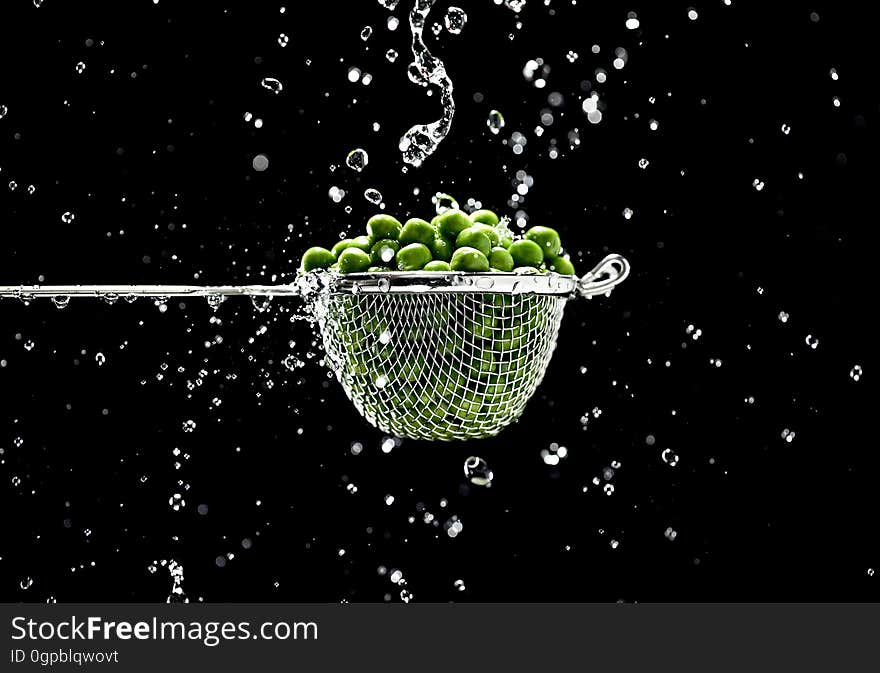 A close up of peas in a metal strainer and water drops around it. A close up of peas in a metal strainer and water drops around it.