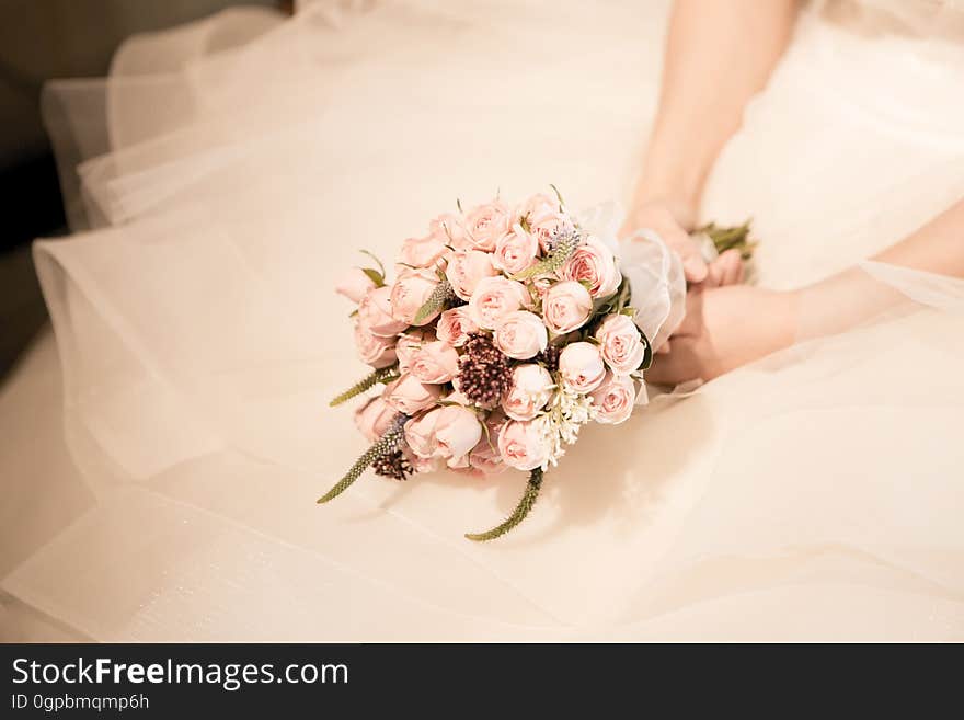 Close up of bride holding bouquet over folds of white gown. Close up of bride holding bouquet over folds of white gown.