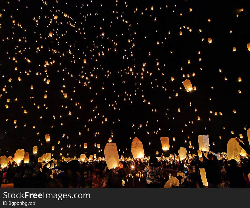 A crowd of people at a celebration and sky lanterns floating in the air.