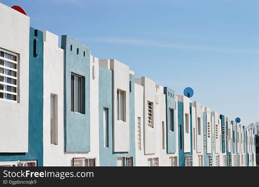 Interesting architectural detail of upper floor of apartment block with outer walls finished in shades of blue and white and with window batons in some of the homes, blue sky. Interesting architectural detail of upper floor of apartment block with outer walls finished in shades of blue and white and with window batons in some of the homes, blue sky.