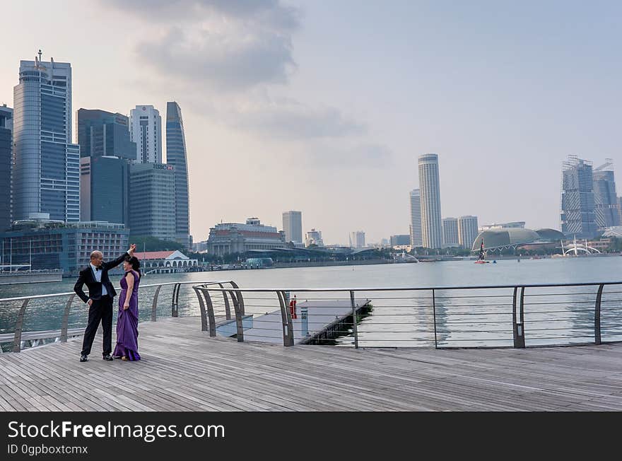 Couple in evening dress on a jetty or riverside decking about to dance, background of river and skyscrapers. Couple in evening dress on a jetty or riverside decking about to dance, background of river and skyscrapers.