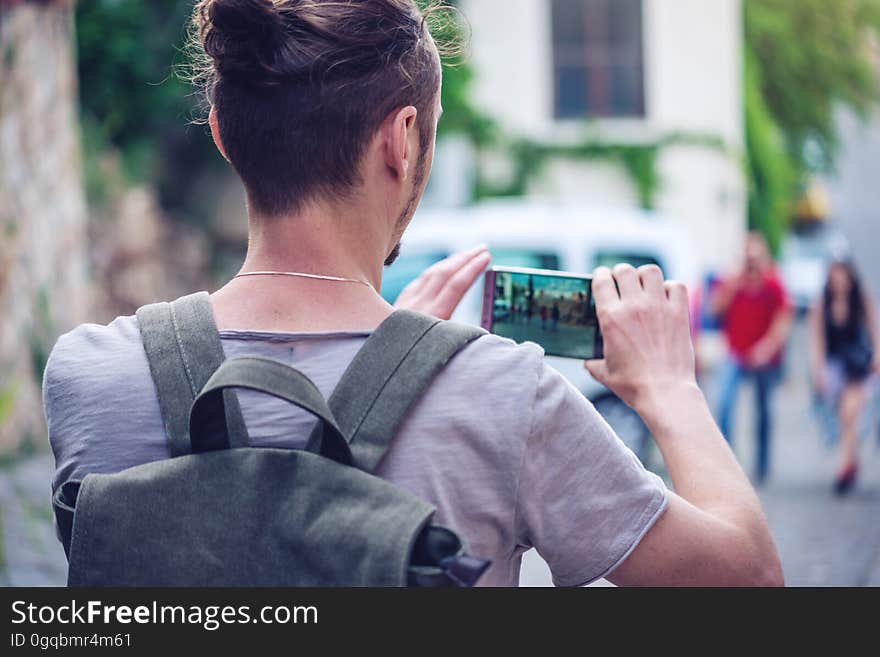 Man backpack makes a photo on your smartphone on a city street