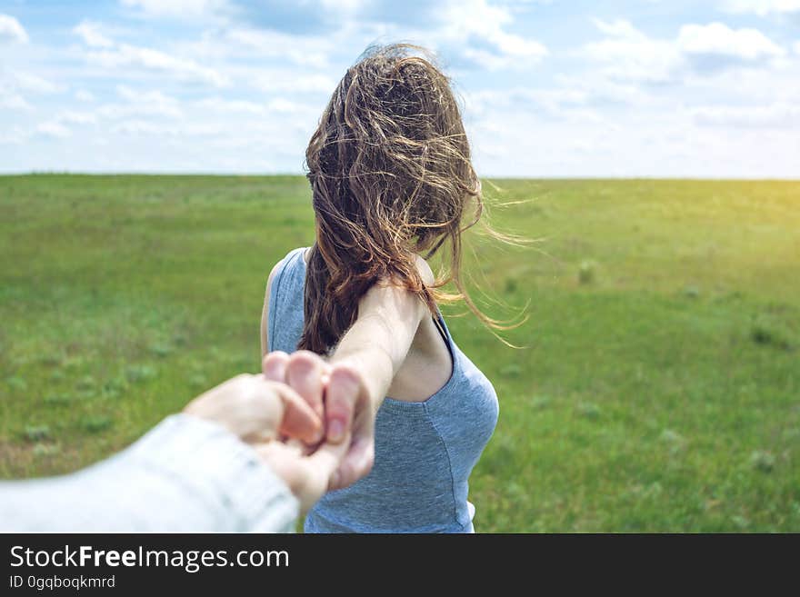 Follow me, Attractive brunette girl holding the hand of the leads in a clean green field, steppe with clouds