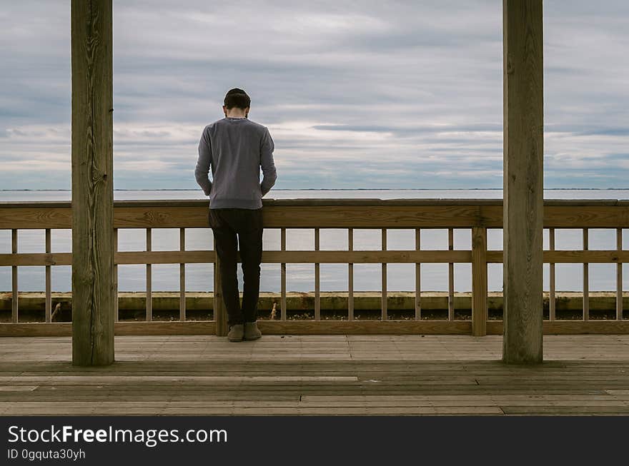 Back of man standing along wooden railing overlooking ocean on sunny day. Back of man standing along wooden railing overlooking ocean on sunny day.