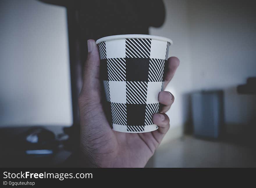 Close up of hand holding brown and white plaid disposable hot beverage cup. Close up of hand holding brown and white plaid disposable hot beverage cup.