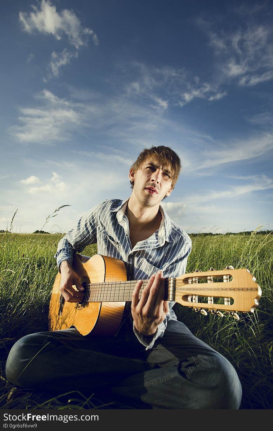 A man playing an acoustic guitar on a field. A man playing an acoustic guitar on a field.