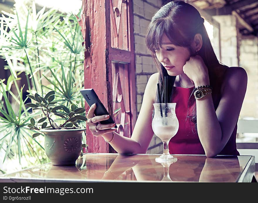 A young woman checking her phone while drinking a beverage.