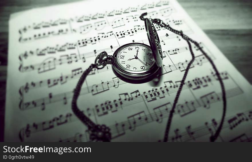 A pocket watch on top of sheet music. A pocket watch on top of sheet music.