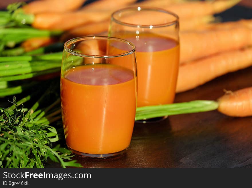 2 Clear Drinking Glass Container with Carrot Juice on Brown Wooden Tabletop in Tilt Shift Lens Photography