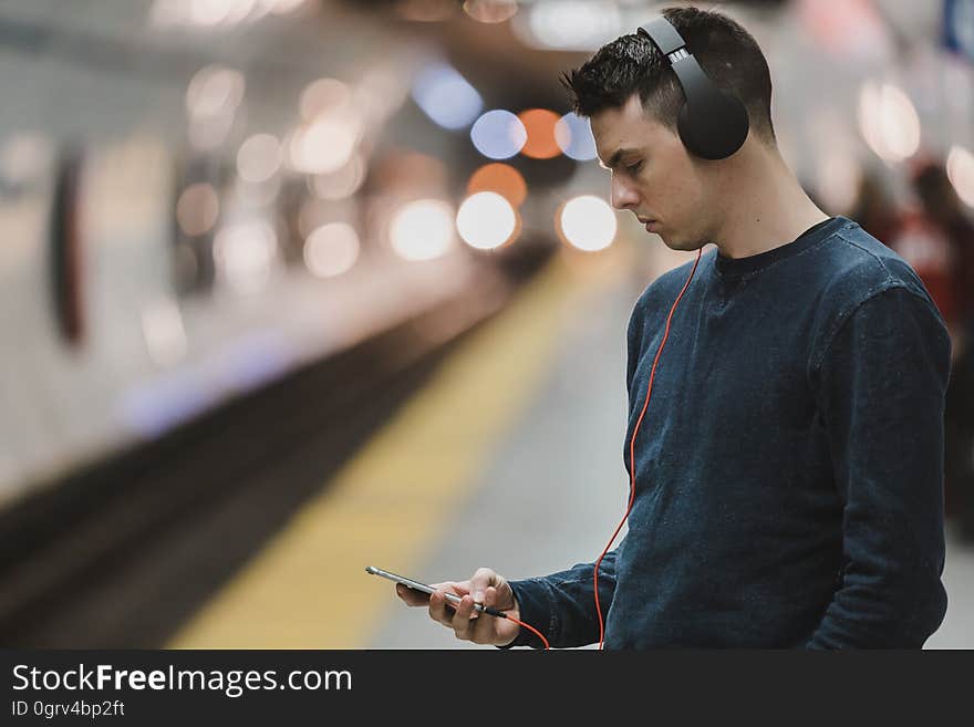 A man waiting for a train or a subway looking at his phone with headphones on. A man waiting for a train or a subway looking at his phone with headphones on.