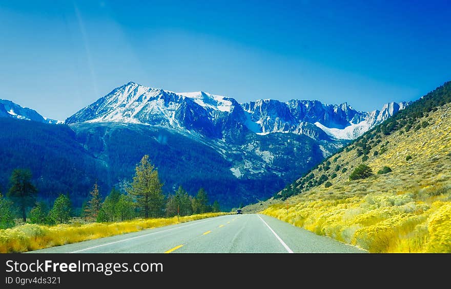 Scenic road through the snow dusted Alpine mountains with fresh green growth on both sides of road, cool blue sky. Scenic road through the snow dusted Alpine mountains with fresh green growth on both sides of road, cool blue sky.