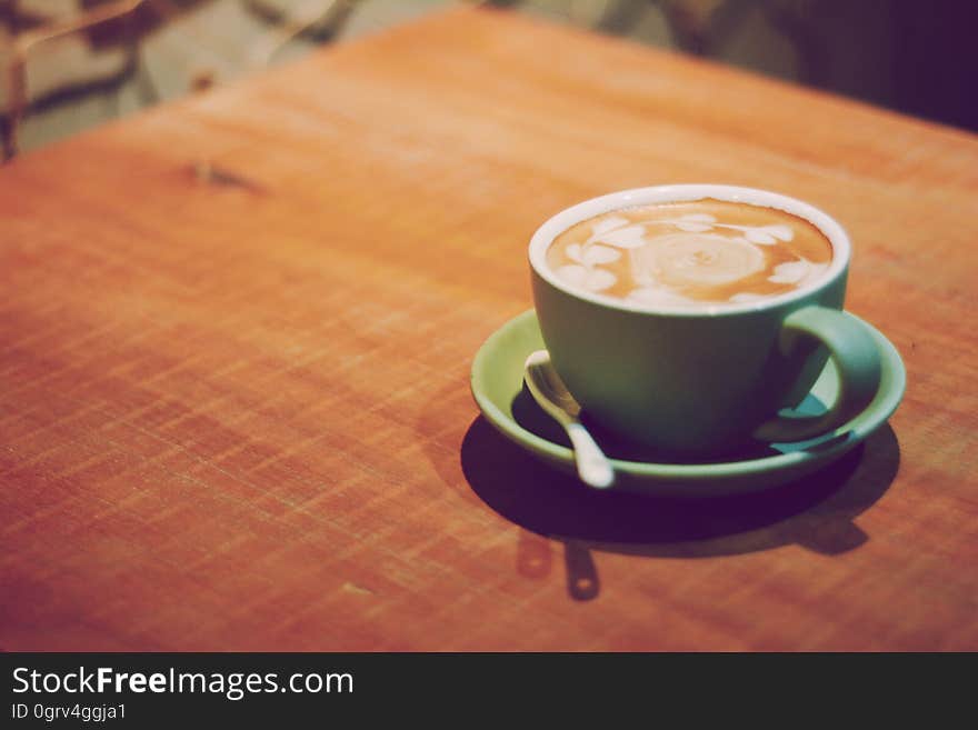 Selective focus on cup of coffee in green cup and saucer with silver spoon. Selective focus on cup of coffee in green cup and saucer with silver spoon.